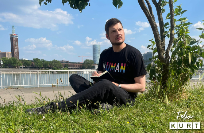 Photo of gay LGBTQ+ queer author Felix Kurt sitting on a riverbank writing for the blog "Writing gay fiction novels with purpose"